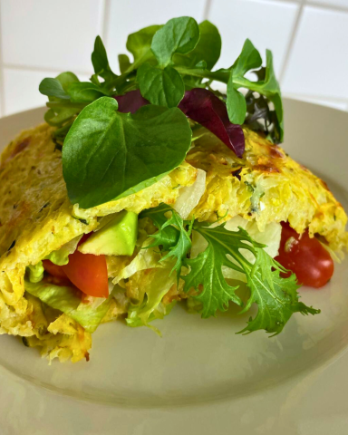 Omelette gefüllt mit Gemüse und frischen Kräutern auf einem Teller.