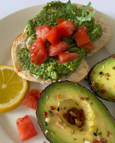 Geröstetes Brot mit Avocado, Tomatenwürfeln und Zitronenscheibe auf einem Teller.